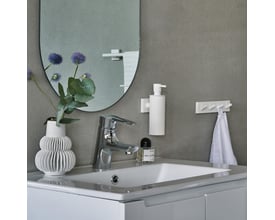 Smedbo House sæbedispenser i mat hvid monteret på en grå betonvæg over en hvid håndvask.