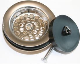 Nærbillede af Viega bundventil dele: messing ventilunderdel med pakninger, rustfri stålsi og sort gummi prop med trekantskrog.