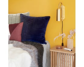 Hübsch Zenith væglampe i messingfarve, monteret over en seng med gule vægge og blå puder.