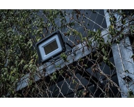 Brennenstuhl 150W LED projektør monteret på en facade med grønne planter og trådnet.