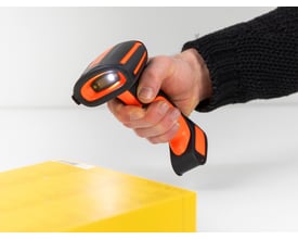 DeLock 1D/2D barcode scanner i hånden, der scanner en gul pakke, med orange og sorte detaljer og en aktiv lysdiode.