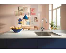 Grohe Blue Pure Startcurve etgrebsbatteri i krom med C-tud monteret ved en køkkenvask med en skål frugt.
