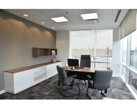 Moderne kontorindretning med skrivebord, stole og hvidt opbevaringsmøbel med trædetaljer foran grå væg.