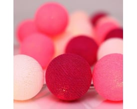 Nærbillede af en Irislights lyskæde med fokus på de teksturerede stofkugler i pink og mørkerød, som udsender et varmt lys.