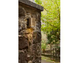 Astro Coastal 7806 Jura Single væglampe monteret på en grov murstensvæg ved indgangen til en have.