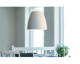 SG Armaturen Pendel Bell Mini i hvid/guld med dybtmonteret lyskilde, hængende over et spisebord i et lyst rum.