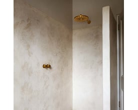 Vola indbygningstermostat med løs afgangsmuffe til hovedbruser og gylden brusehoved monteret på rå, lys væg.