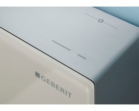 Geberit Monolith Plus cisternemodul med front i sandgrå glas og børstet aluminium.