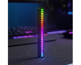 RGBIC musiklampe i mørkt rum, lyser op med farvede søjler foran et gaming-setup med tastatur og mus.