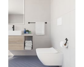 Smedbo Cube enkel håndklædestang i mat sort, monteret på en badeværelsesvæg over en toiletkumme med håndklæder.