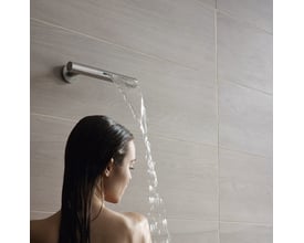 Vola vandfaldsbruser i matsort finish monteret på væg med trælook-fliser, mens vandet løber ned over en kvinde.