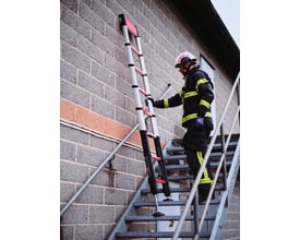 Brandmand bruger en rød teleskopstige Rescue på 3,5 m ved en murstensbygning og en udendørs trappe.