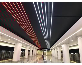 Ansell Lighting U-Cell LED strip i 6500K hvid og rød lys på en sort loftbeklædning i et moderne offentligt rum med søjler.