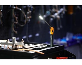 Ironside genopladelig slim mini LED-håndlampe lyser på et værkstedsbord med det justerbare lampehoved vinklet.