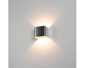 SLV MANA lampeskærm monteret på en grå væg, oplyst med et varmt lys der skaber lysstriber opad og nedad.