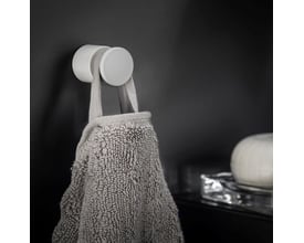 Cosmic håndklædekrog i mat hvid, vist monteret på en mørk væg med et gråt håndklæde hængende på.