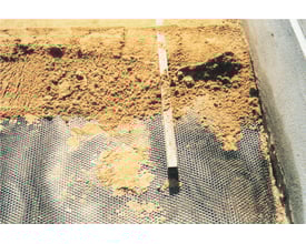 Expo-net armeringsnet 1211L påbegyndt monteret på sandet underlag med en vaterpas og grus foran.