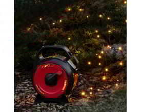 Konstsmide lyskæde med 150 ravfarvede lys på kabeltromle, placeret i en have med tændte lys i buske.