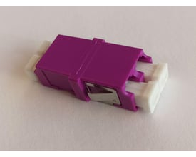 Adapter OM4 LC/PC Duplex i lilla med SC footprint og uden flange. Den har hvide LC-porte på hver side og et metalklemme til montering.