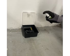 Person i arbejdshandske sprayer Camro monitoreringsspray ind i en lukket rottefælde.