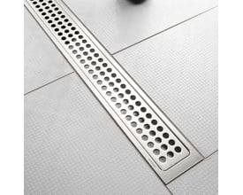 Unidrain fritliggende afløbsarmatur på 1200mm i bejdset stål, monteret i et badeværelsesgulv med grålige fliser.