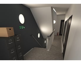 Ansell Lighting Mercurial IP54 loftlampe monteret i en trappeopgang med nødudgangsskilt og brandslukker i baggrunden.