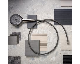 Hansgrohe håndbruserslange i sort krom ligger snoet på en grå marmorbordplade sammen med fliser og stofprøver.