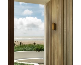Astro Coastal Jura Twin væglampe monteret på en træbeklædt facade ved havet, med udsigt til strand og himmel.