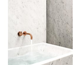Vola Sc4 2-grebsblander i messingfarve, monteret på marmoreret væg med vandløb ned i et marmoreret badekar.