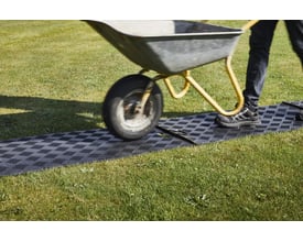 En trillebør kører hen over en Letbæk Plast gangplade lagt på en græsplæne.