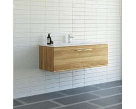 Dansani Mido møbelpakke på 121 cm med varm eg-finish og en skuffe, monteret på en hvid væg i et moderne badeværelsesmiljø med fliser.