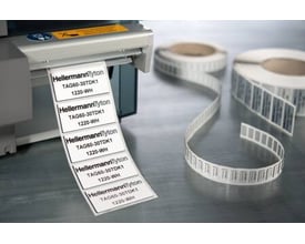 Hvide HellermannTyton-panelmærker på rulle, 45 x 15 mm, ses med trykte markeringer ved en labelprinter.
