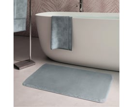 HeFe FUZZY bademåtte i grå, 400x600 mm, placeret på et lyst badeværelsesgulv ved siden af et fritstående badekar.