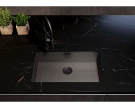 Blanco Infino afløb i sort mat rustfrit stål indbygget i en mørk køkkenbordplade med hane og grønne planter i baggrunden.