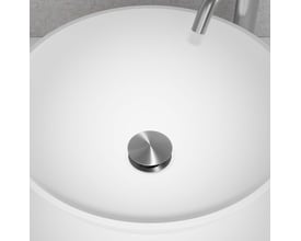 Primy Steel Duo Pop-up bundventil i børstet stål monteret i en hvid håndvask, med synlig vandhane i baggrunden.