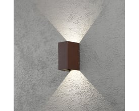 Konstsmide Cremona væglampe i rustent aluminium, monteret på en grå væg og udsender lys op og ned.