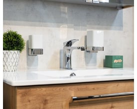 Smedbo ice sæbedispenser i poleret krom og hvidt porcelæn placeret ved siden af en vandhane på en vask.