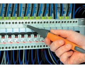 Elma Instruments PR400 testprobe med fjernbetjening, holdt i hånden ved en eltavle med mange ledninger og afbrydere.