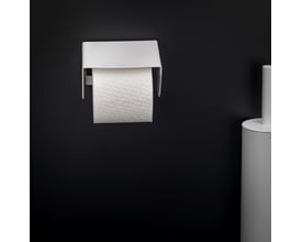 Fron view af Cosmic toiletpapirholder i mat hvid med låg, monteret på sort væg, klar til brug med en rulle toiletpapir.