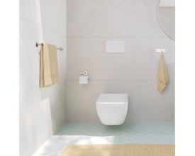 Smedbo Cube toiletpapirholder monteret på væggen i et moderne badeværelse med toilet og håndklæder.