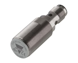 Carlo Gavazzi induktiv aftaster M18, PNP NC og 12 mm, med kort, skærmet sølvfarvet gevindhus set skråt forfra.