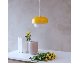 Dyberg Larsen HAIPOT pendel i gul, monteret over et bord med gul blomsterdekoration og lysegrå vase.