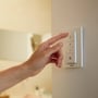 En hånd trykker på Hue Dimmer switch på væggen, som styrer Philips Hue Being loftslampe.