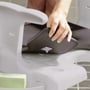 En hånd monterer et gråt, blødt sæde på en hvid Etac Swift toiletstol for øget komfort.