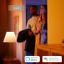 Par i et farverigt oplyst hjem med symboler for Alexa og Google Assistant, som Philips Hue Being kan bruges med.