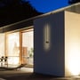 Moderne V-TAC LED væglampe monteret på en facade ved en terrasse med udendørs møbler, oplyst om aftenen.