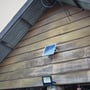 Solpanel LED projektør fra V-TAC monteret på en træbeklædt væg under et bølgebliktag.