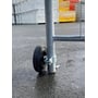 Hjul til dørelement med 200 mm diameter, monteret på et gråt metaldørspost på en våd asfaltoverflade med lagerbygninger i baggrunden.