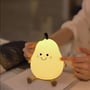Den tændte MOCHI pæreformede natlampe står på en bog, mens en finger rører ved den bløde overflade.
