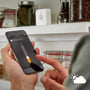 En hånd holder en smartphone, der viser Philips Hue appens indstillinger for sensorens lysfølsomhed, med et tiltalende køkken i baggrunden.
